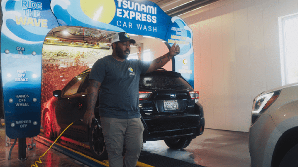 Cars entering the car wash tunnel while being greeted by an employee.